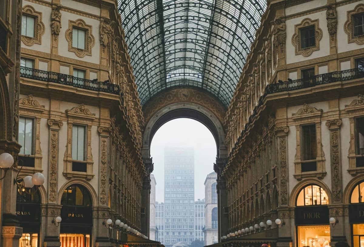 Elegancka galeria ze szklaną kopułą w Galleria Vittorio Emanuele II w Mediolanie, otoczona ekskluzywnymi sklepami i butikami, przywołująca luksus i architektoniczną wspaniałość.