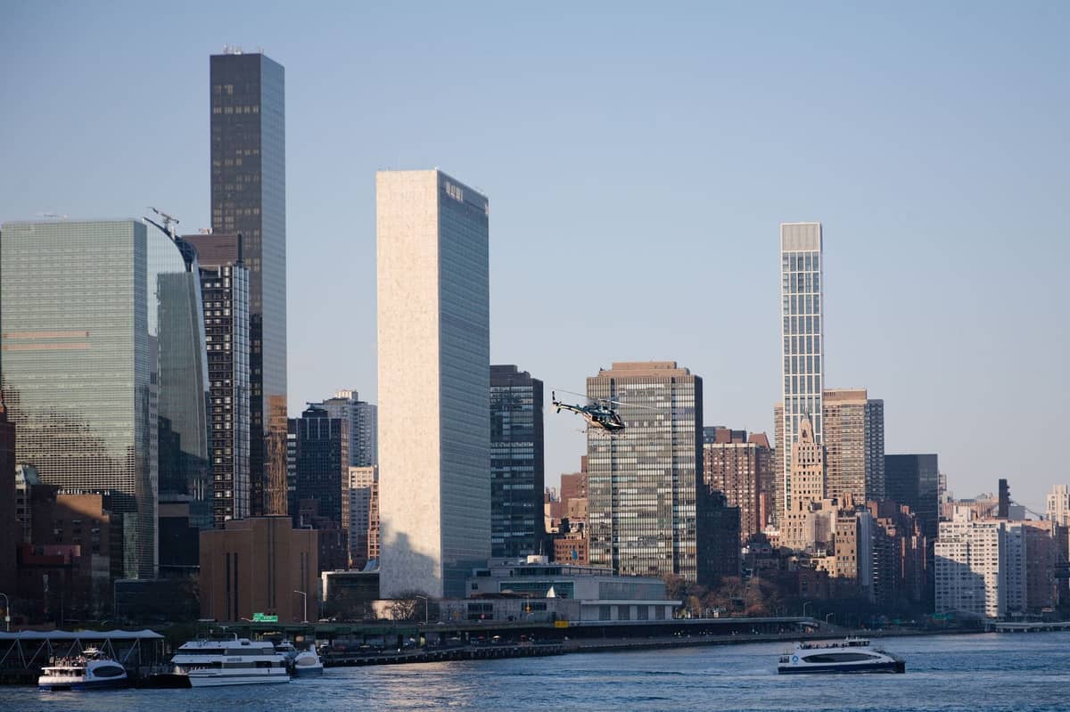 Hubschrauber fliegt über den East River mit den Wolkenkratzern von New York City und Yachten auf dem Wasser bei Tag