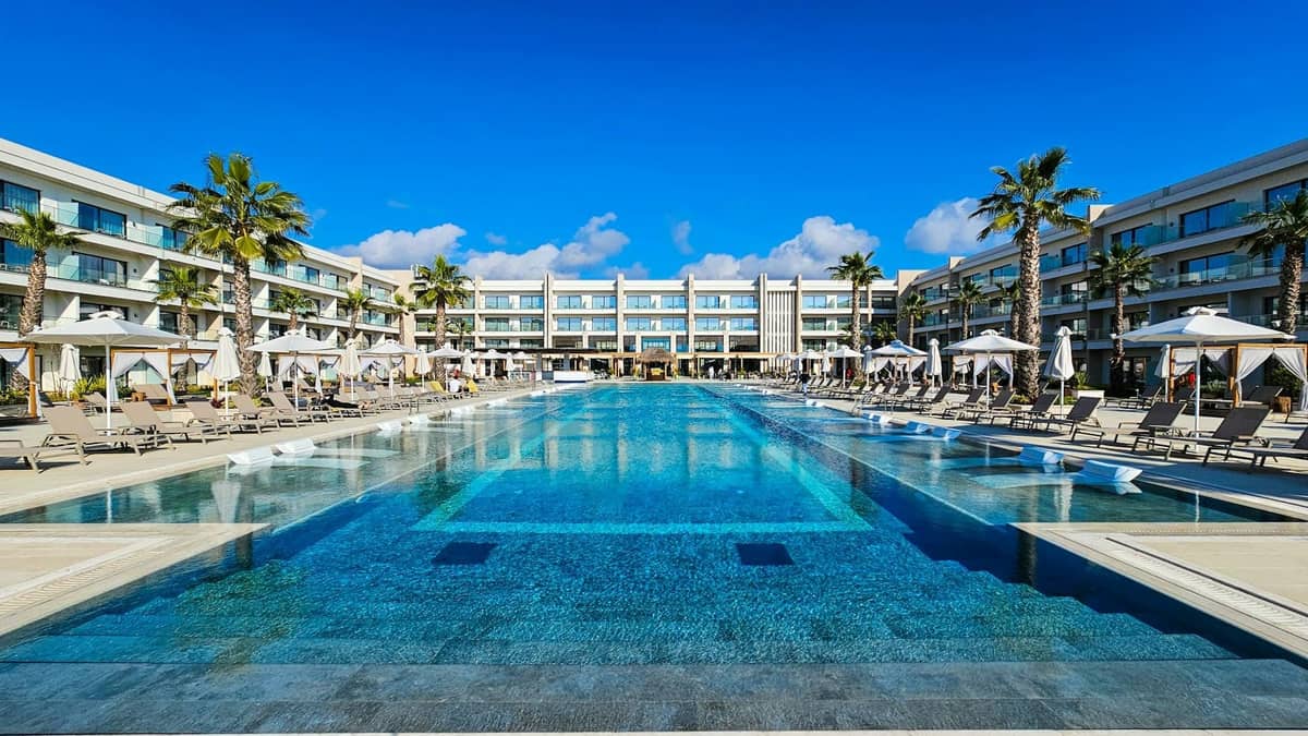 Luxurious modern beachfront hotel with large swimming pool, sun loungers, palm trees, and blue sky, representing upscale accommodations in Rhodes.