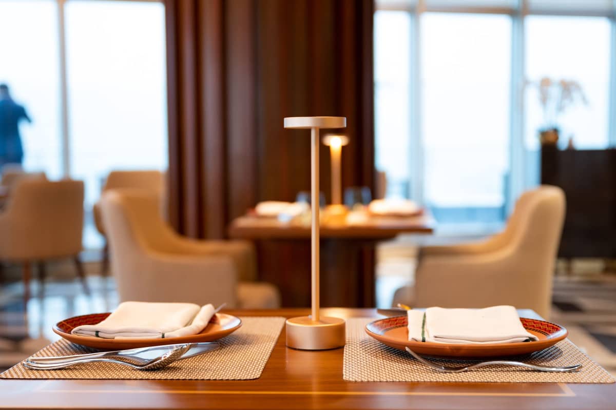 Mesa de jantar elegante para dois em um restaurante sofisticado, com cadeiras confortáveis, vista panorâmica da cidade por janelas amplas e decoração moderna e minimalista.