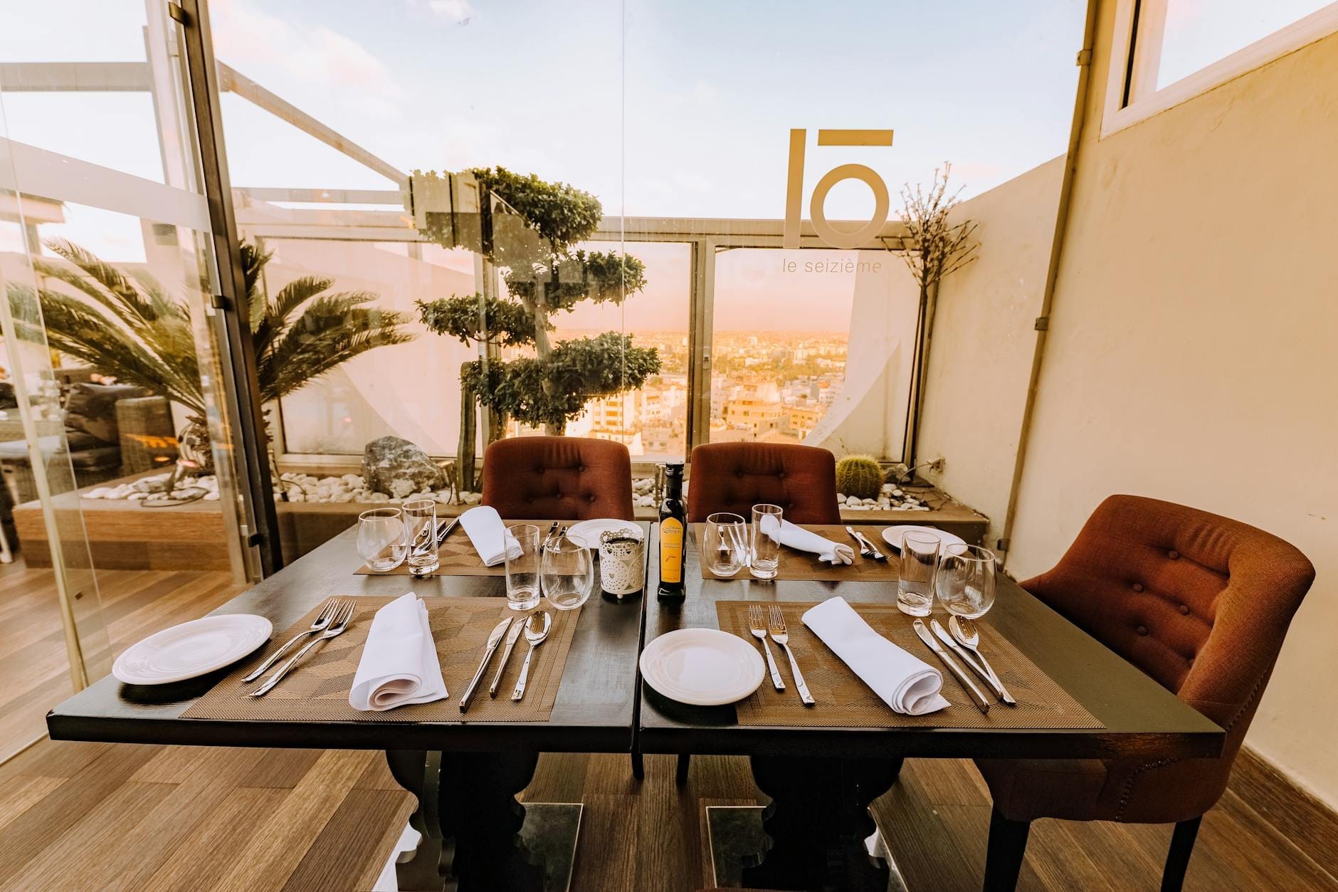 Eleganter Restauranttisch für vier Personen gedeckt mit Stadtblick durch Glasfenster, braunen Stühlen, Gläsern und ordentlich arrangierten Servietten.