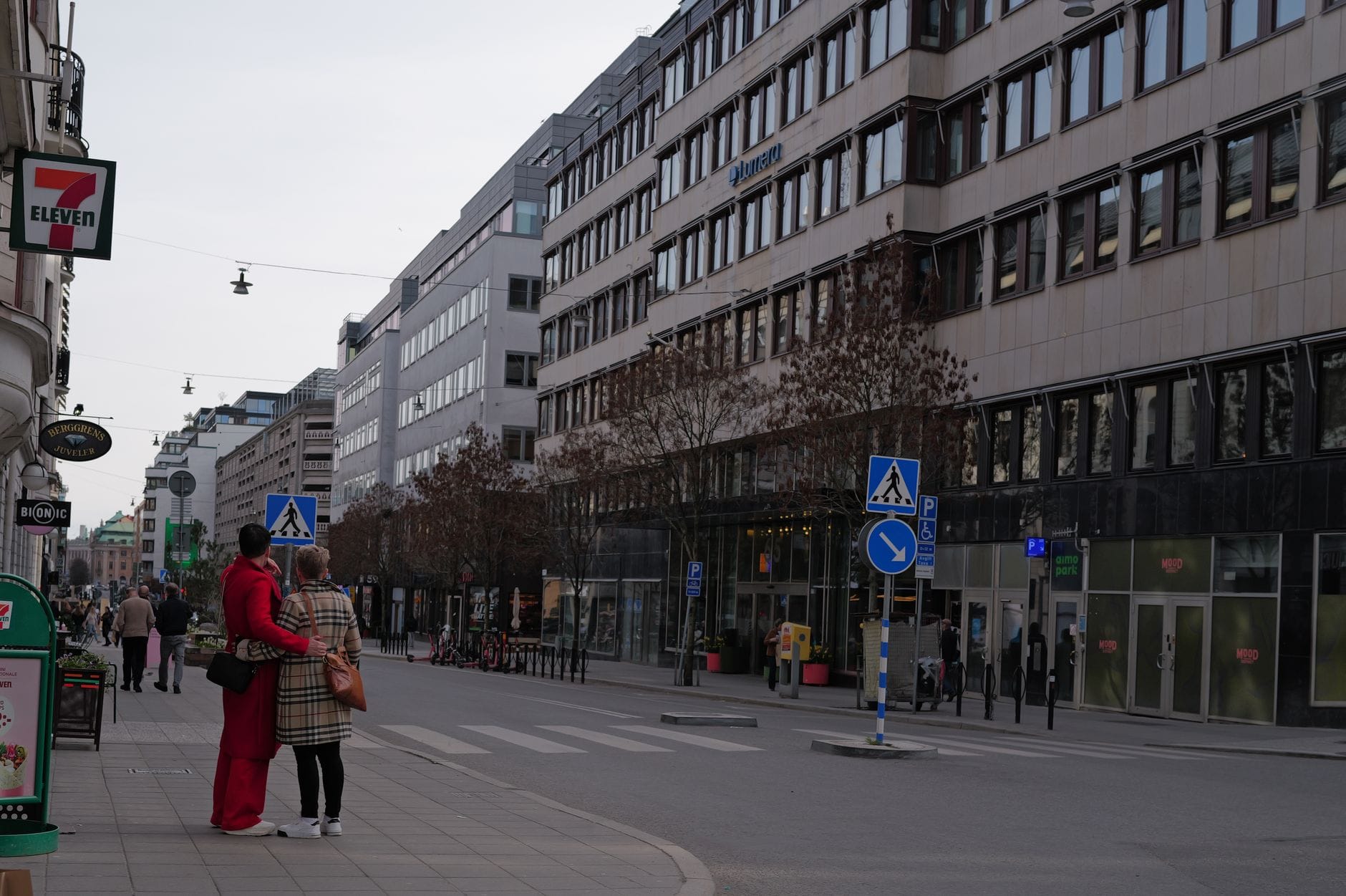 ถนนกว้างทันสมัยในย่าน Östermalm ของ Stockholm พร้อมร้านค้าระดับหรู ผนังกระจก และผู้คนที่เดินผ่านไปมา