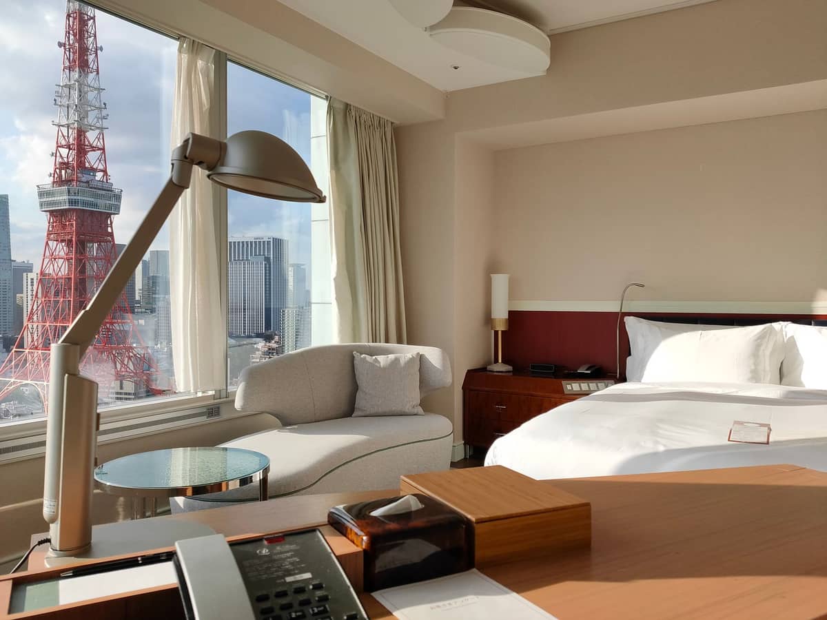 Bright, modern Tokyo hotel room with a view of Tokyo Tower through the window, showing comfortable bed and lounge chair.