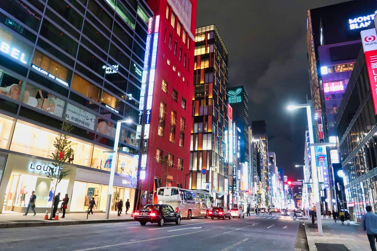 View of Ginza, Tokyo's most luxurious shopping district, featuring upscale store fronts, glowing lights, and modern high-rise buildings at night.