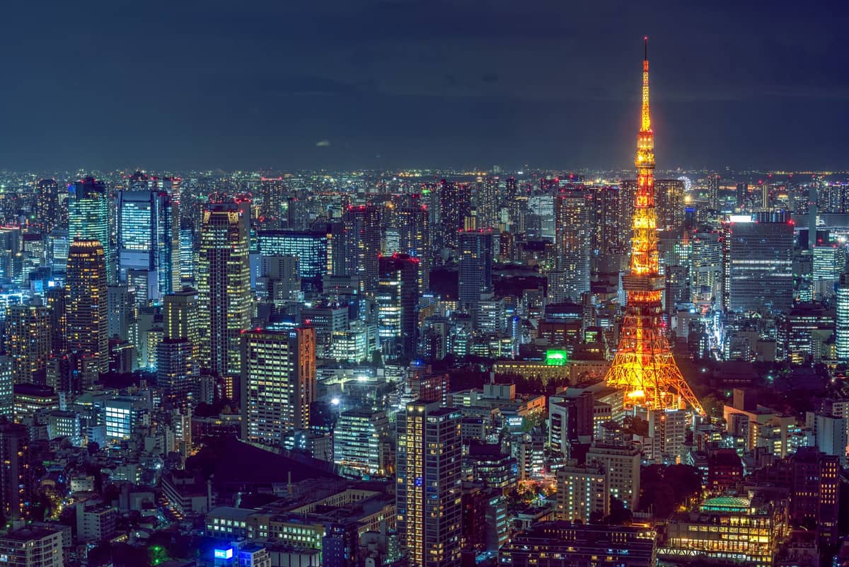 Illuminated Tokyo Tower glowing among high-rise buildings at night, spectacular cityscape showcasing central Tokyo's skyline and urban luxury ambiance.