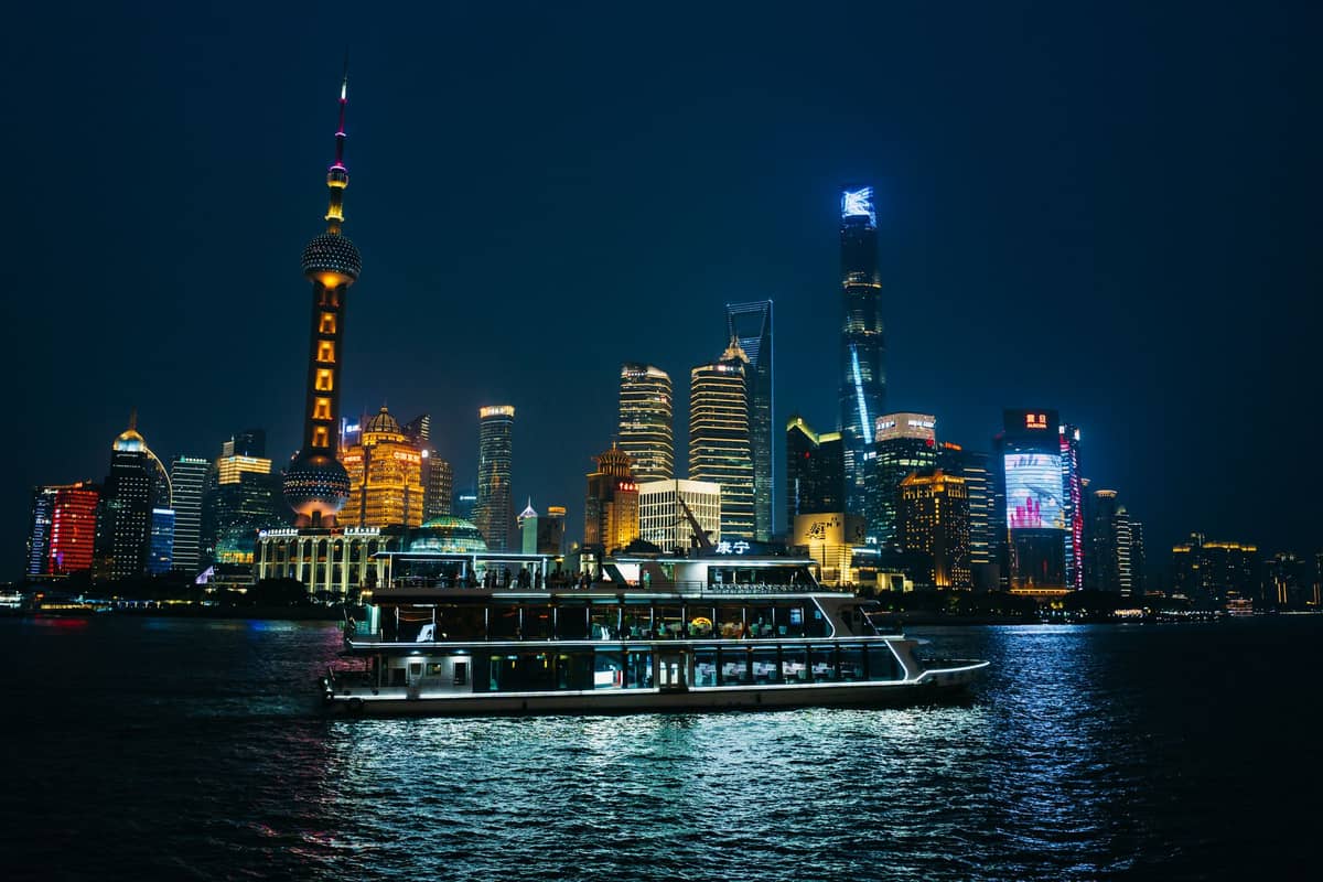 Ein luxuriöses Yachtboot fährt nachts auf dem Huangpu-Fluss mit Shanghais ikonischer Skyline, einschließlich des Oriental Pearl Tower, der hell erleuchtet im Hintergrund erstrahlt.