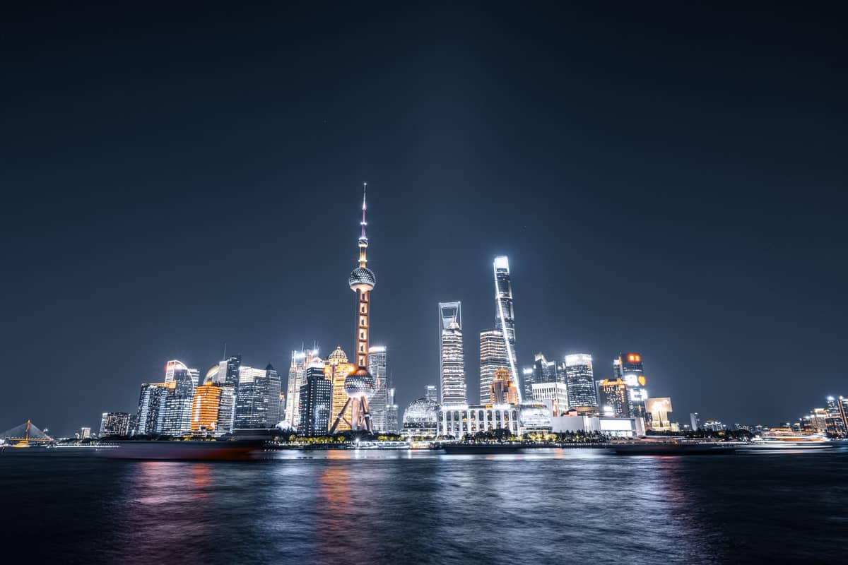 Nächtlicher Blick auf die Shanghaier Skyline mit beleuchteten Wolkenkratzern am Bund, die sich im Huangpu-Fluss spiegeln – ein Sinnbild für modernen Luxus und urbane Eleganz.