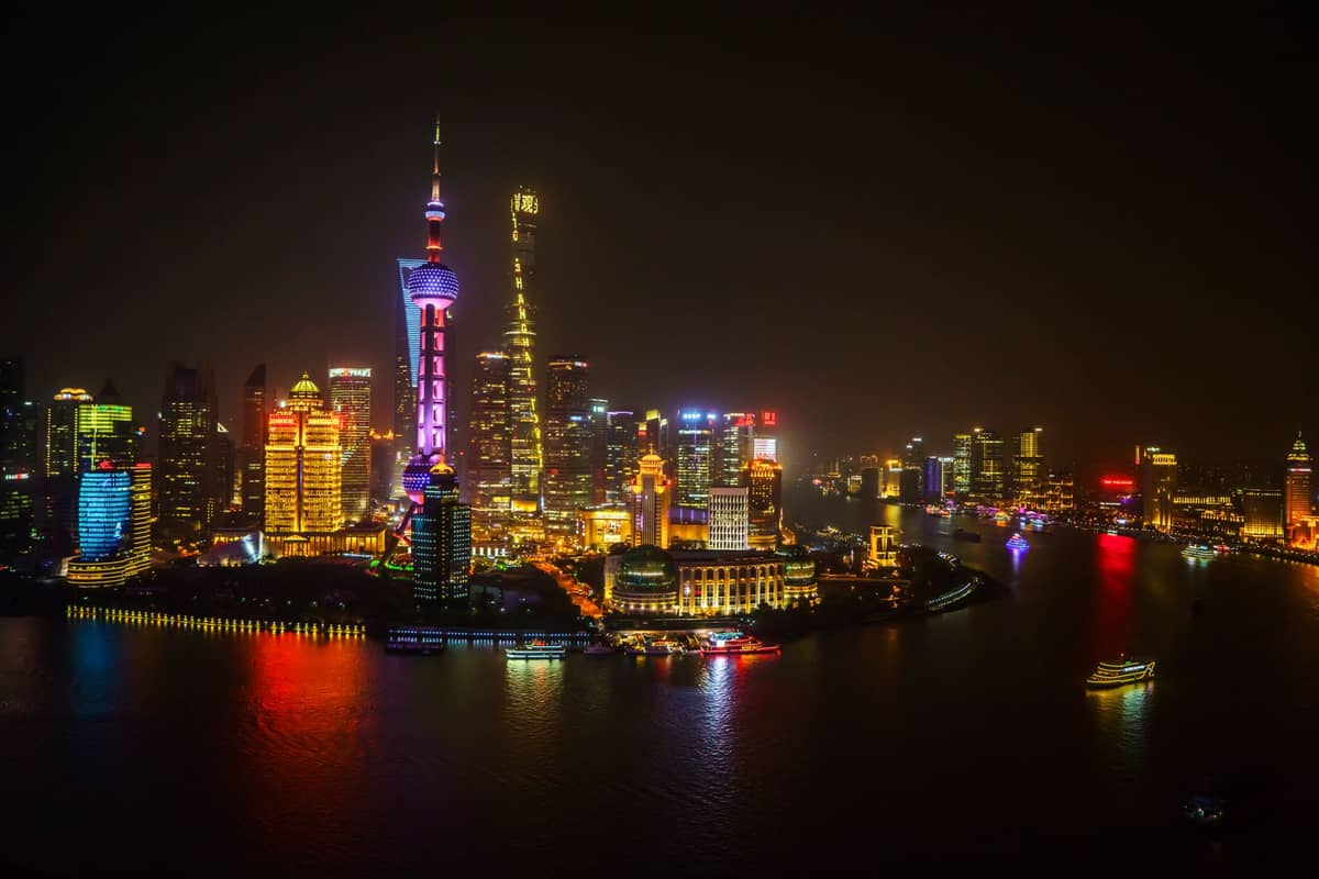 Skyline von Shanghai bei Nacht mit hell erleuchteten Wolkenkratzern, dem Oriental Pearl Tower und bunten Spiegelungen auf dem Huangpu.