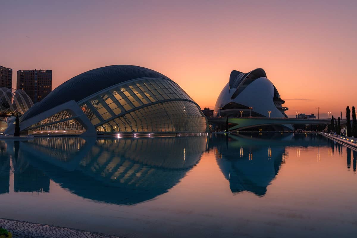 Valencia'daki Ciudad de las Artes y las Ciencias'ın fütüristik cam ve beyaz binaları, gün batımında durgun suda yansıyor.