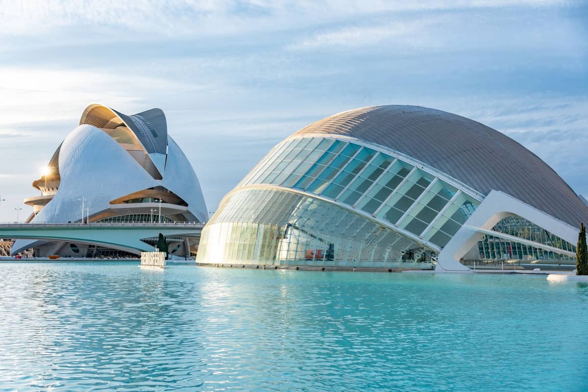 Vista panoramica della Ciudad de las Artes y las Ciencias a Valencia, con i suoi edifici dall'architettura moderna circondati da piscine turchesi sotto un cielo blu.