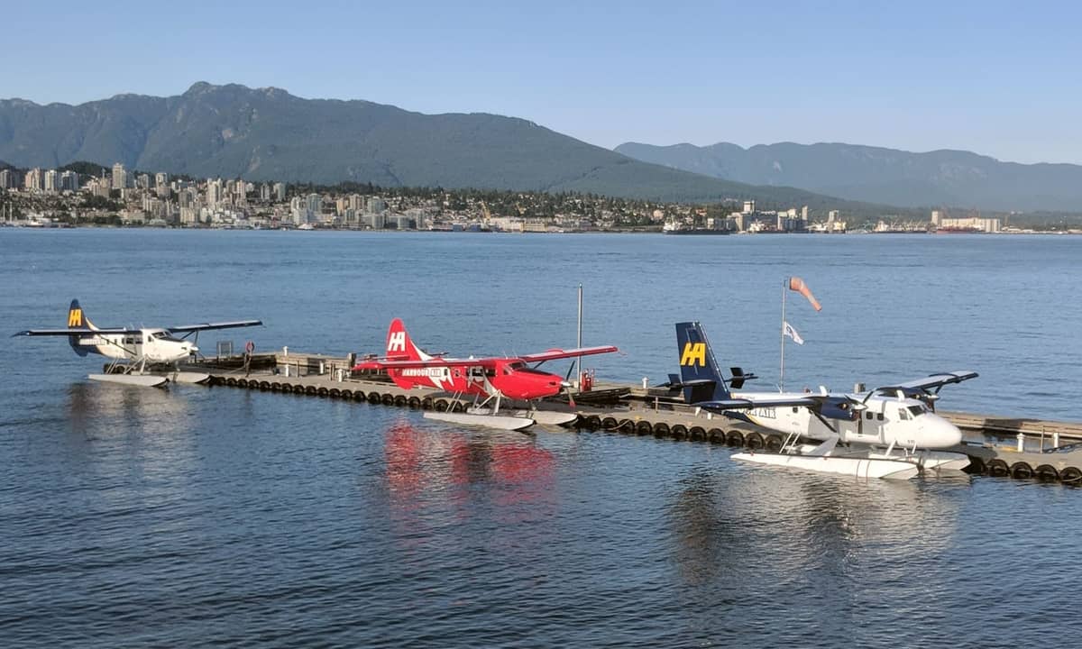 เครื่องบินทุ่นลอยน้ำจอดเทียบท่าที่ Vancouver Harbour พร้อมวิวเส้นขอบฟ้าของเมืองและเทือกเขา North Shore เป็นฉากหลังในวันที่ท้องฟ้าแจ่มใส