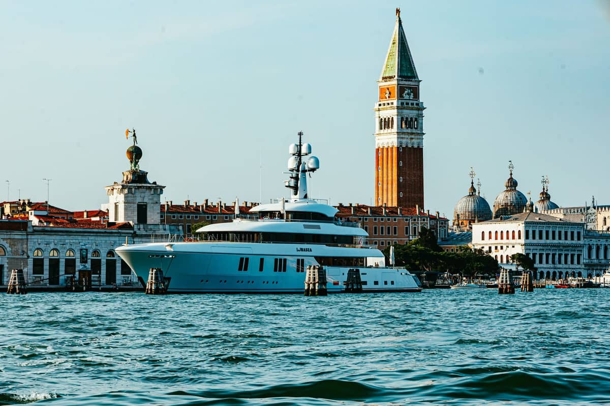 Eine Luxusyacht vor dem ikonischen Campanile di San Marco und den historischen Palazzi am Canal Grande in Venedig bei Sonnenuntergang.