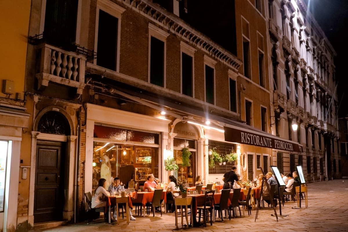 Abendliches Essen im Freien im Ristorante Pedrocchi in Venedig, mit Tischen voller Gäste, die unter warmem Licht vor einem historischen Gebäude speisen.