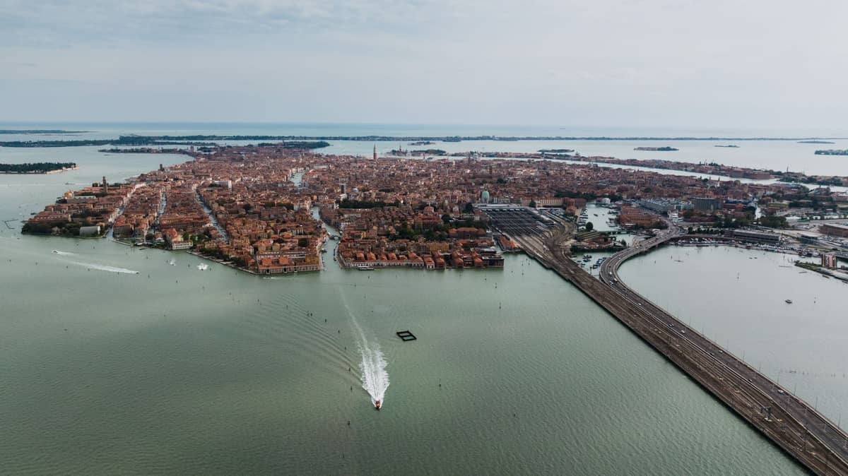 Weitläufige Luftaufnahme von Venedig mit seinen zahlreichen Inseln, Kanälen und der Abwesenheit von Autos, mit Booten auf der Lagune und sichtbarer Eisenbahnlinie.