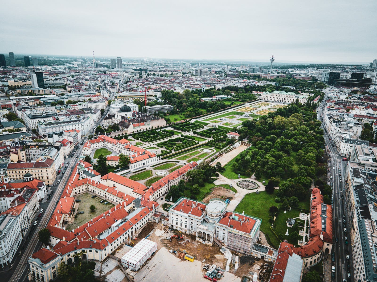 Vista aerea del maestoso Palazzo del Belvedere di Vienna e dei suoi giardini formali circondati dall'architettura cittadina, che mostrano lusso ed eleganza imperiale.