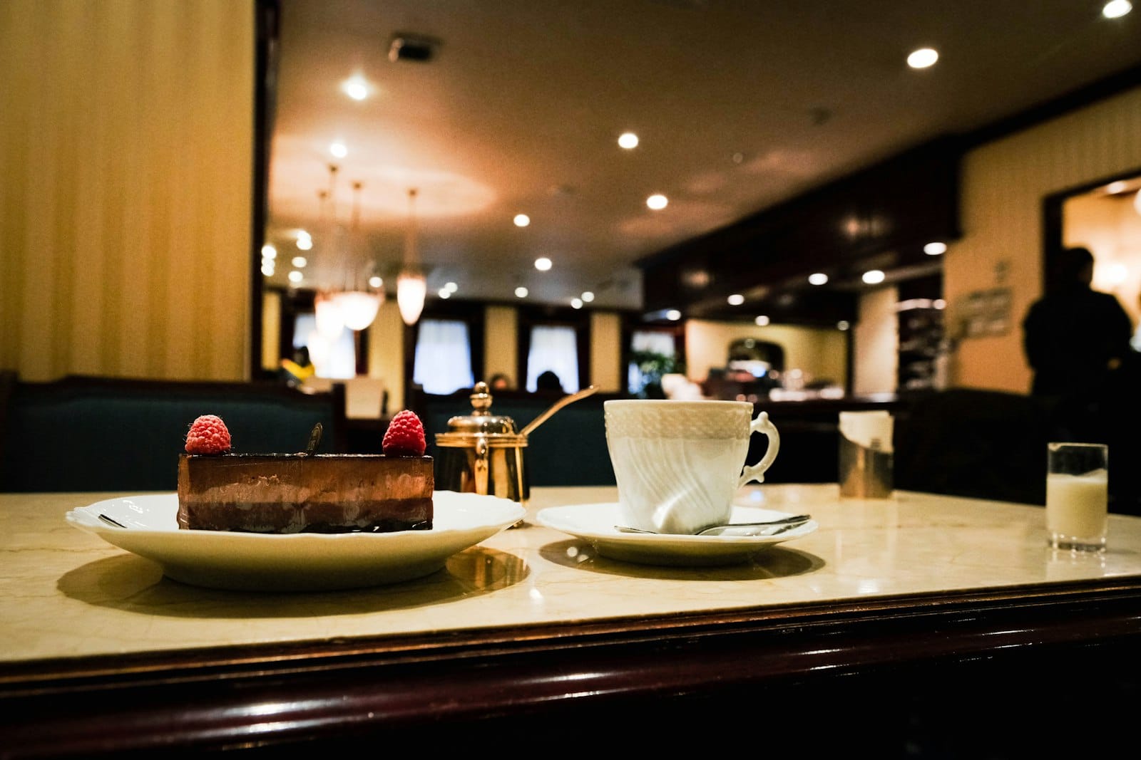 Elegante tavolo da caffè con dolce al cioccolato, tazza di caffè e stoviglie dorate in un classico ristorante europeo dall'atmosfera calda.