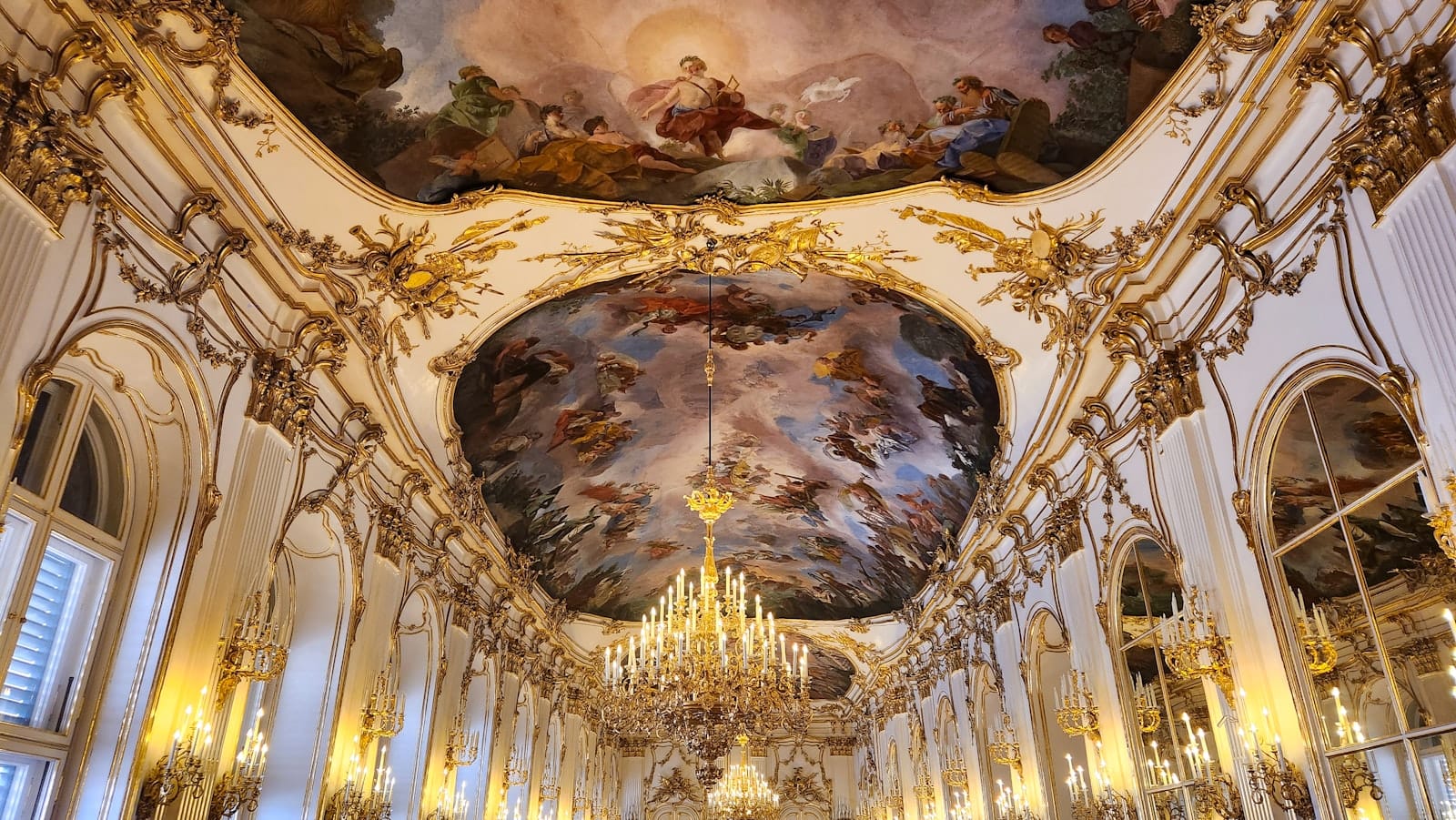 Prunkvoll dekorierter barocker Palaissaal in Wien mit vergoldeten Verzierungen, funkelnden Kronleuchtern und einer eindrucksvollen bemalten Decke – ein Sinnbild für kaiserliche Grandeur und Luxus.