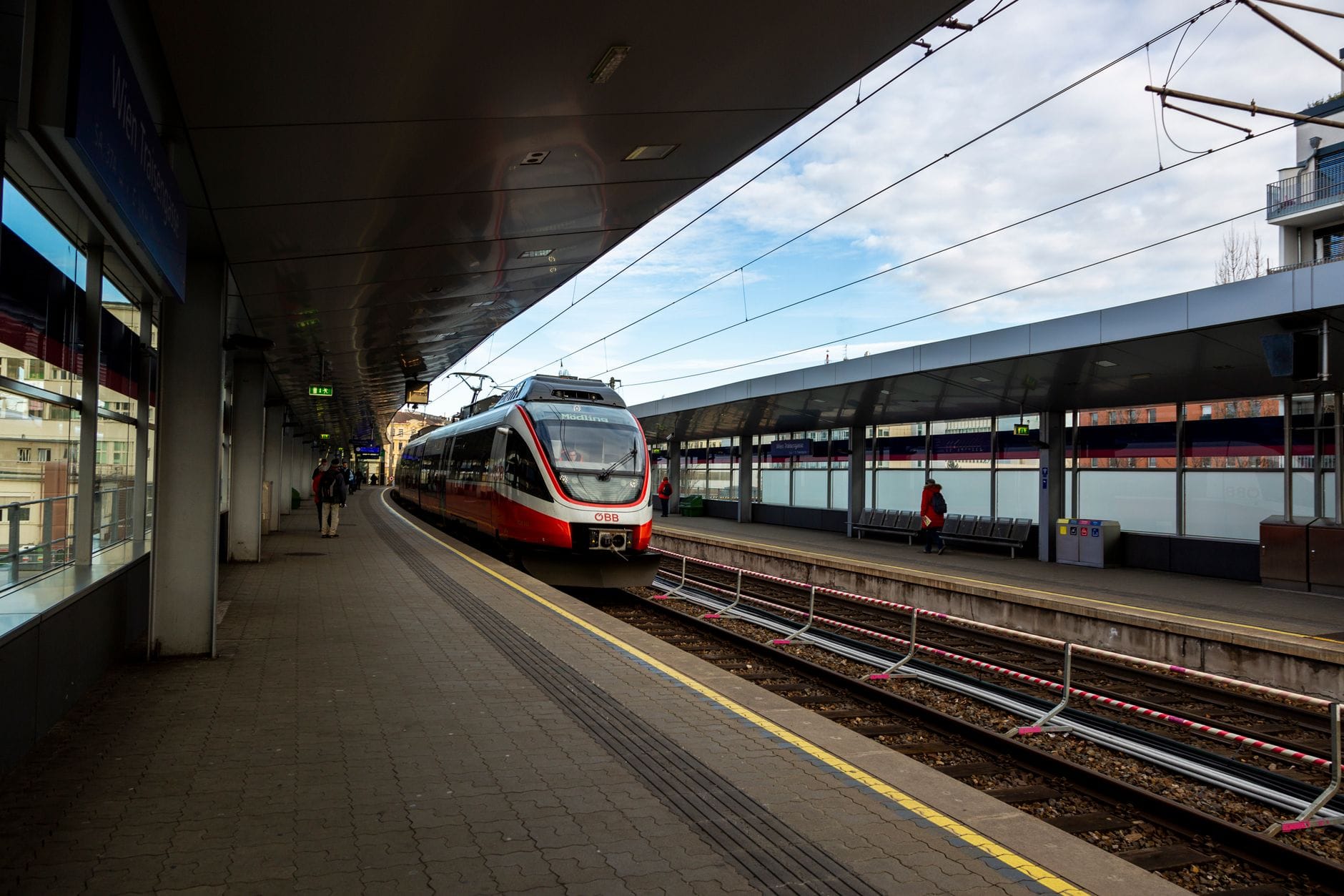 Moderno treno rosso e bianco della S-Bahn o treno regionale in arrivo su un binario ben curato della stazione ferroviaria di Vienna durante il giorno.