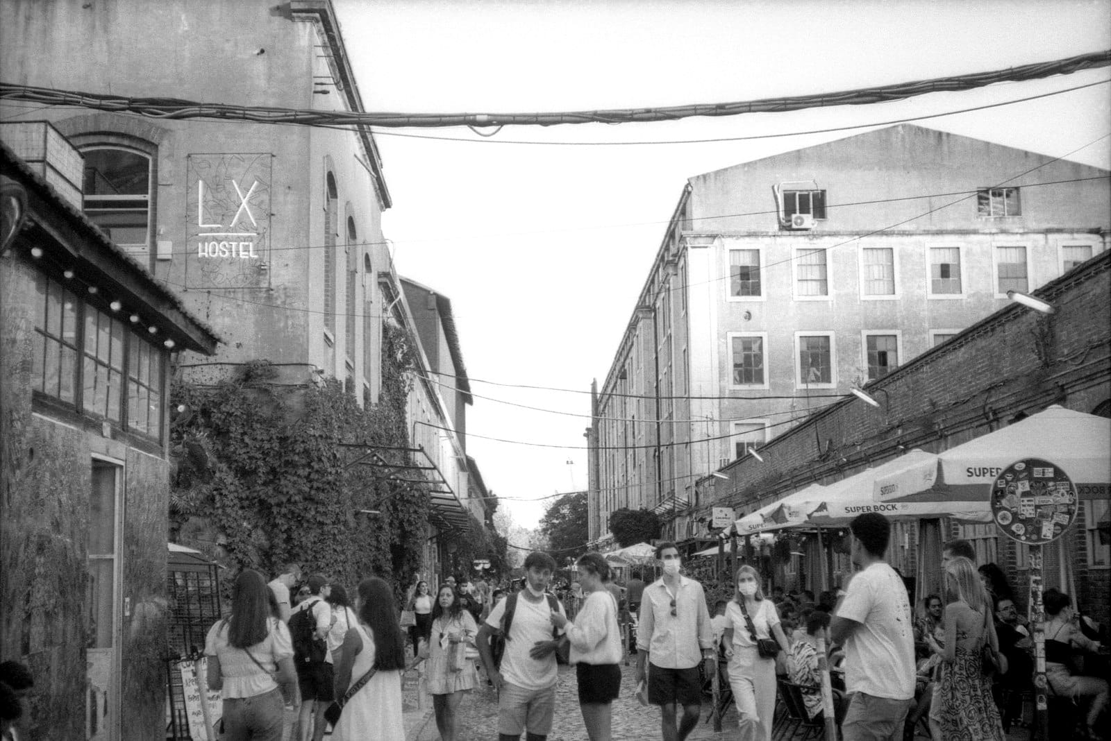 Il vivace cortile di LX Factory con persone che esplorano negozi, storici edifici industriali, sedute all'aperto e insegne creative nel quartiere culturale di Lisbona.