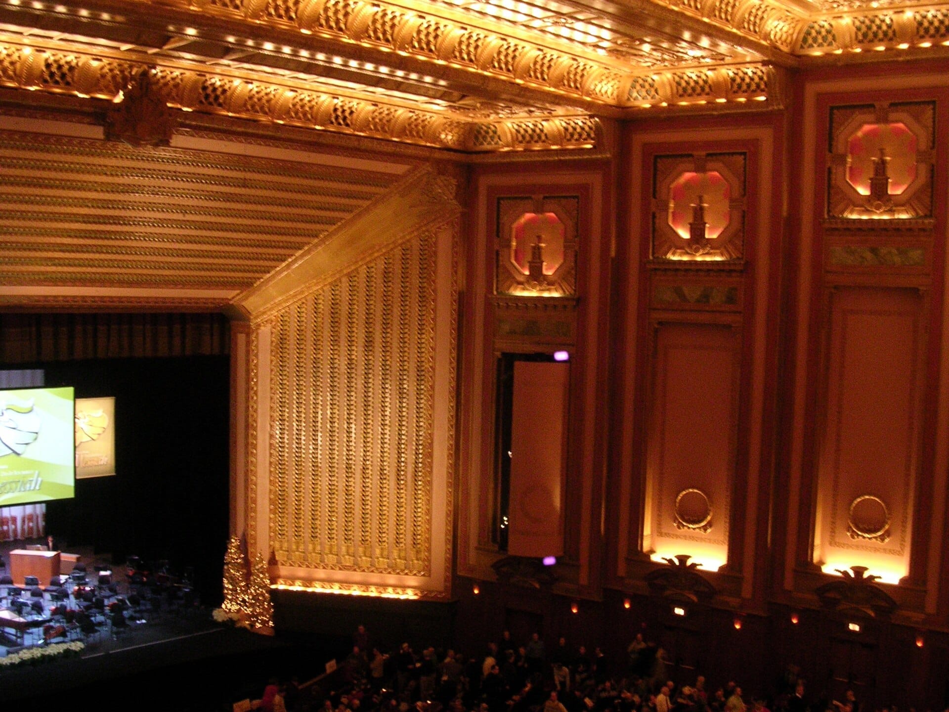 Grandioso interno del Lyric Opera of Chicago con ornate pareti dorate, palcoscenico allestito, illuminazione scenografica e spettatori in cerca dei propri posti.