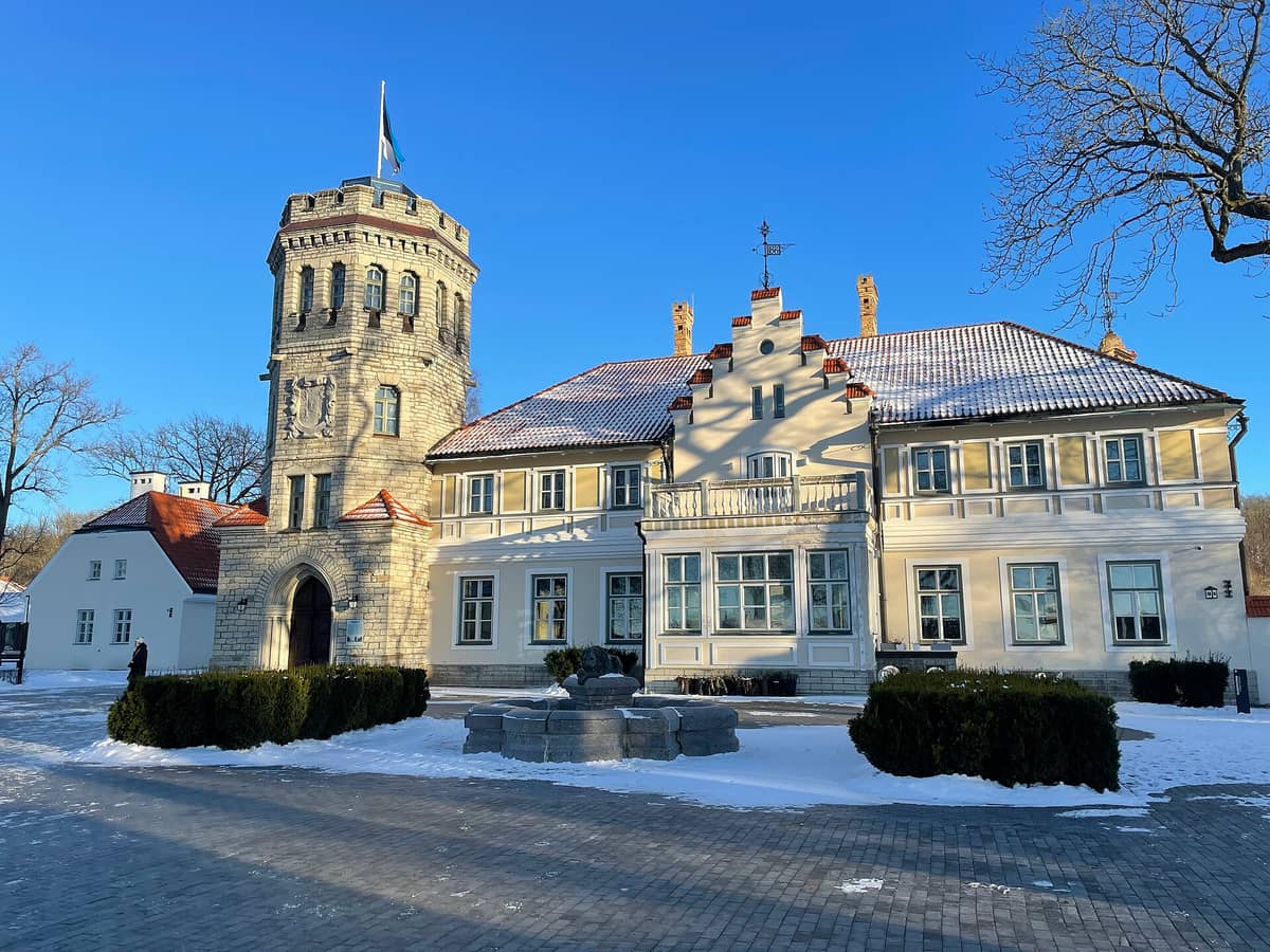 Schloss Maarjamäe in Tallinn von vorne, mit seinem markanten neugotischen Turm, der hellgelben Fassade, schneebedecktem Gelände und klarem blauem Himmel.
