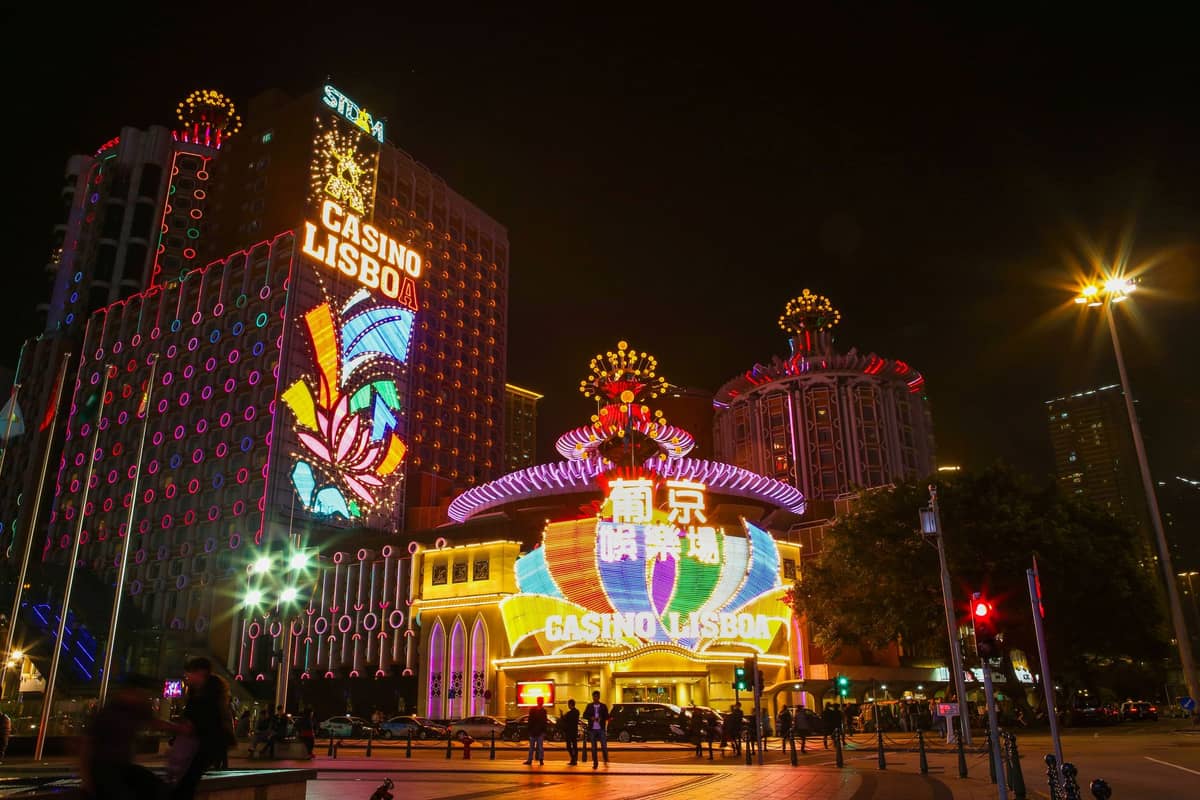 Hell erleuchtetes Casino Lisboa in Macau bei Nacht mit Menschenmassen davor und blendenden Neonlichtern, die für die Kasinolandschaft der Stadt einzigartig sind.
