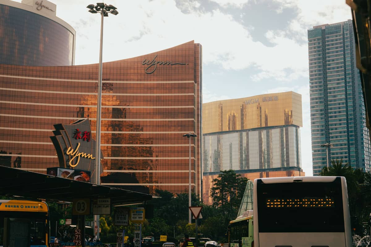Ein Bus wartet an einer Haltestelle vor dem Wynn Macau Resort mit anderen Kasinogebäuden im Hintergrund bei Tageslicht.