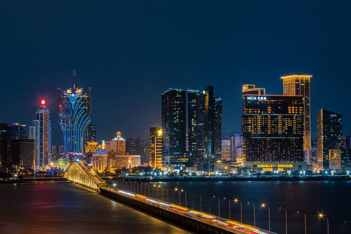 Nachtansicht der Skyline von Macau mit den hell erleuchteten Casinos Grand Lisboa und MGM Macau, gesehen von einer Autobahnbrücke über dem Wasser.