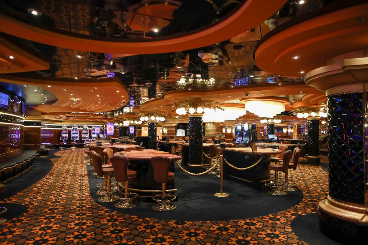 Weitwinkelansicht eines luxuriösen Casinobodens mit mehreren Spieltischen und Spielautomaten, elegantem Licht und aufwendiger Dekoration.