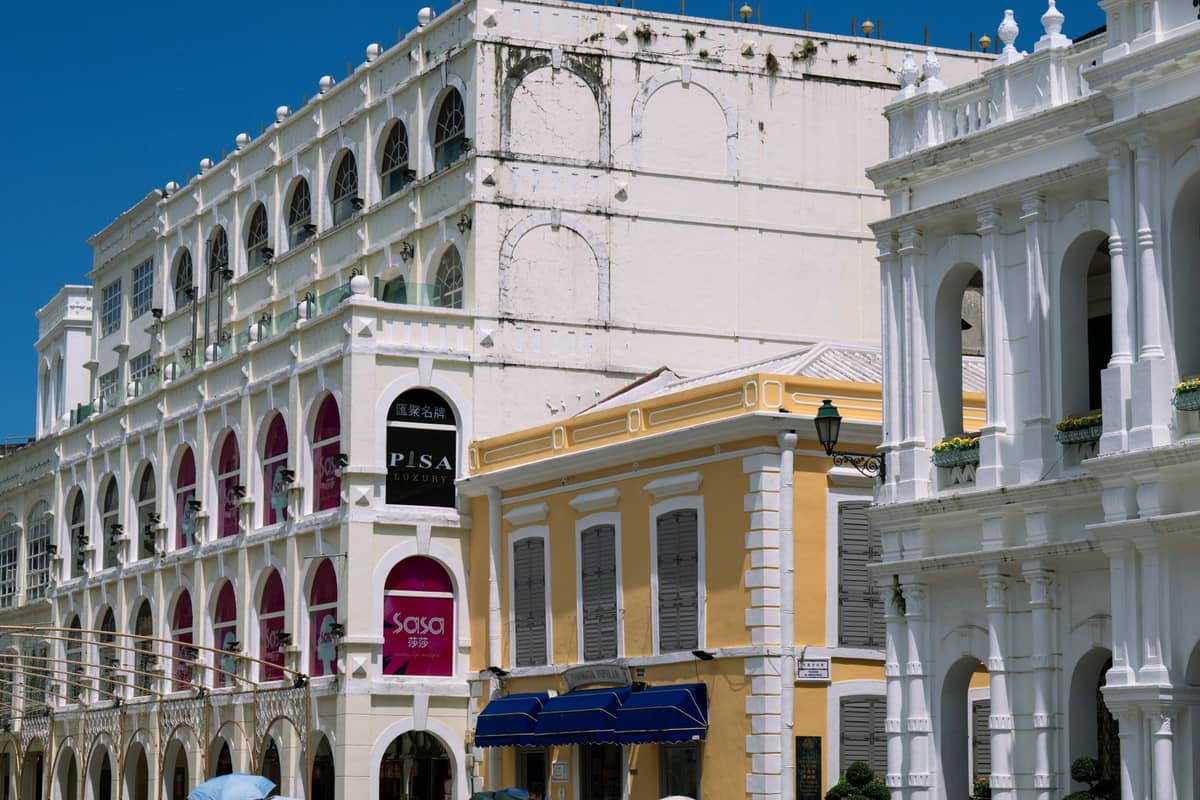 Kolonialstil-Gebäude entlang einer Fußgängerstraße im Zentrum von Macau, mit hellen Fassaden und Arkaden unter klarem blauem Himmel.
