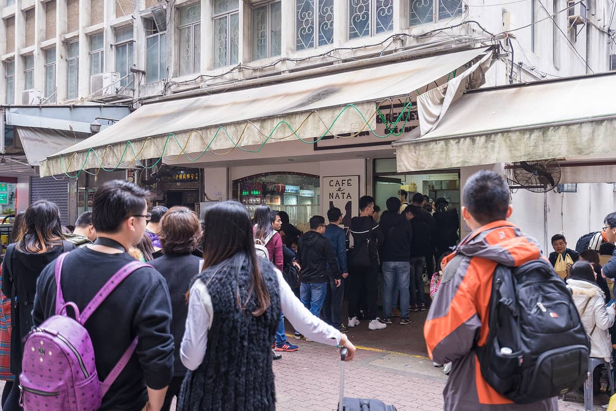 Menschenmenge, die sich vor dem Margaret's Café e Nata anstellt, mit dem Eingang und dem Schild des Cafés gut sichtbar in Macau.