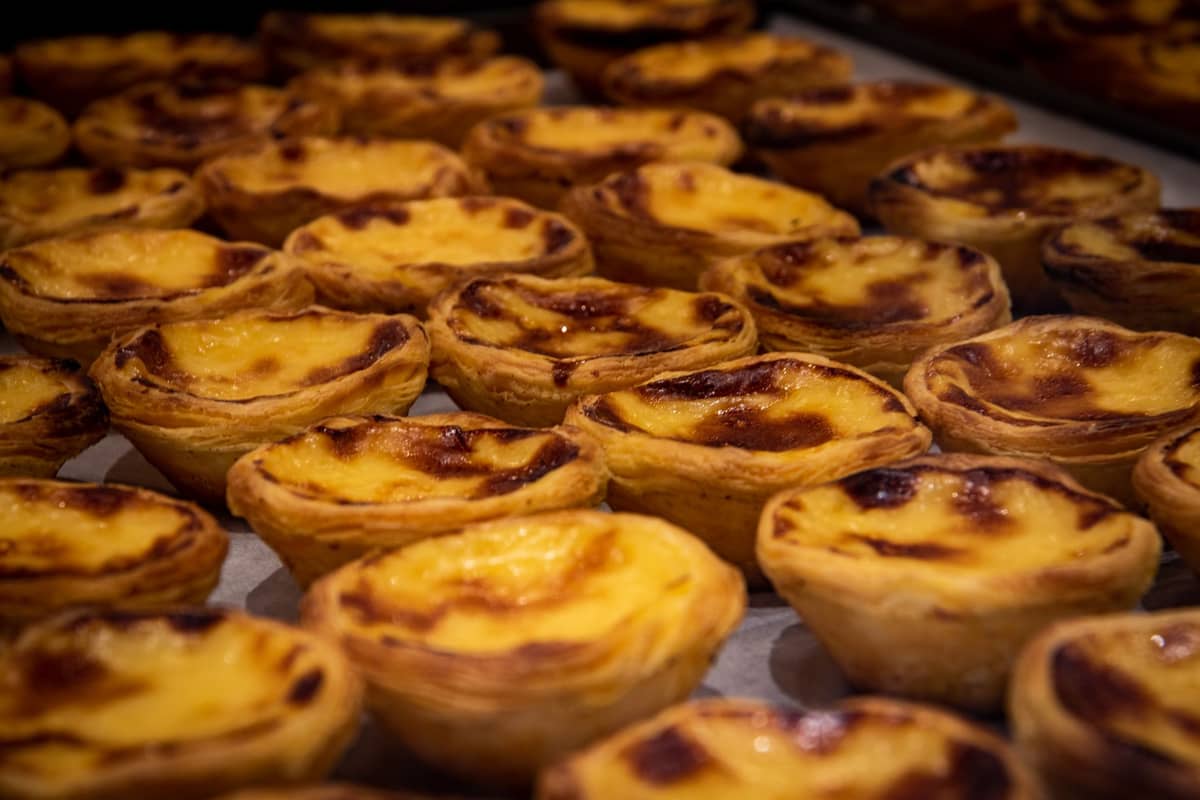 Ein großes Tablett mit Dutzenden Macau-Puddingtörtchen im portugiesischen Stil – goldener Blätterteig mit leicht angebrannten Oberflächen, frisch und bereit zum Essen.