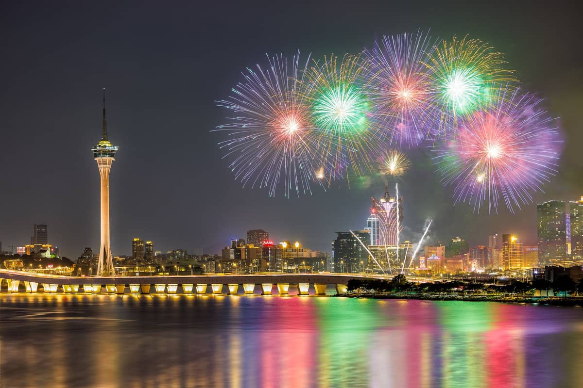 Feuerwerk über der Skyline von Macau bei Nacht – mit dem Macau Tower, den beleuchteten Stadtgebäuden und deren Spiegelung im Wasser.