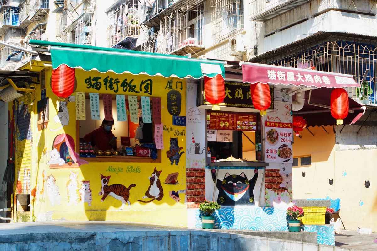 Zwei bunte Straßenimbissstände in Macau, geschmückt mit Laternen und illustrierten Schildern, vor lokalen Wohngebäuden.