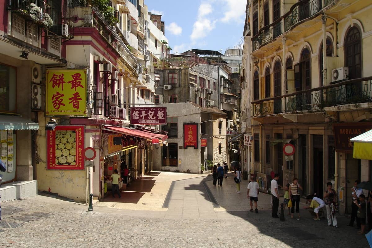 Straßenszene in Macau mit portugiesischer Architektur, enger gepflasterter Gasse und Schildern lokaler Restaurants, die auf ein romantisches Restaurantviertel hindeuten.