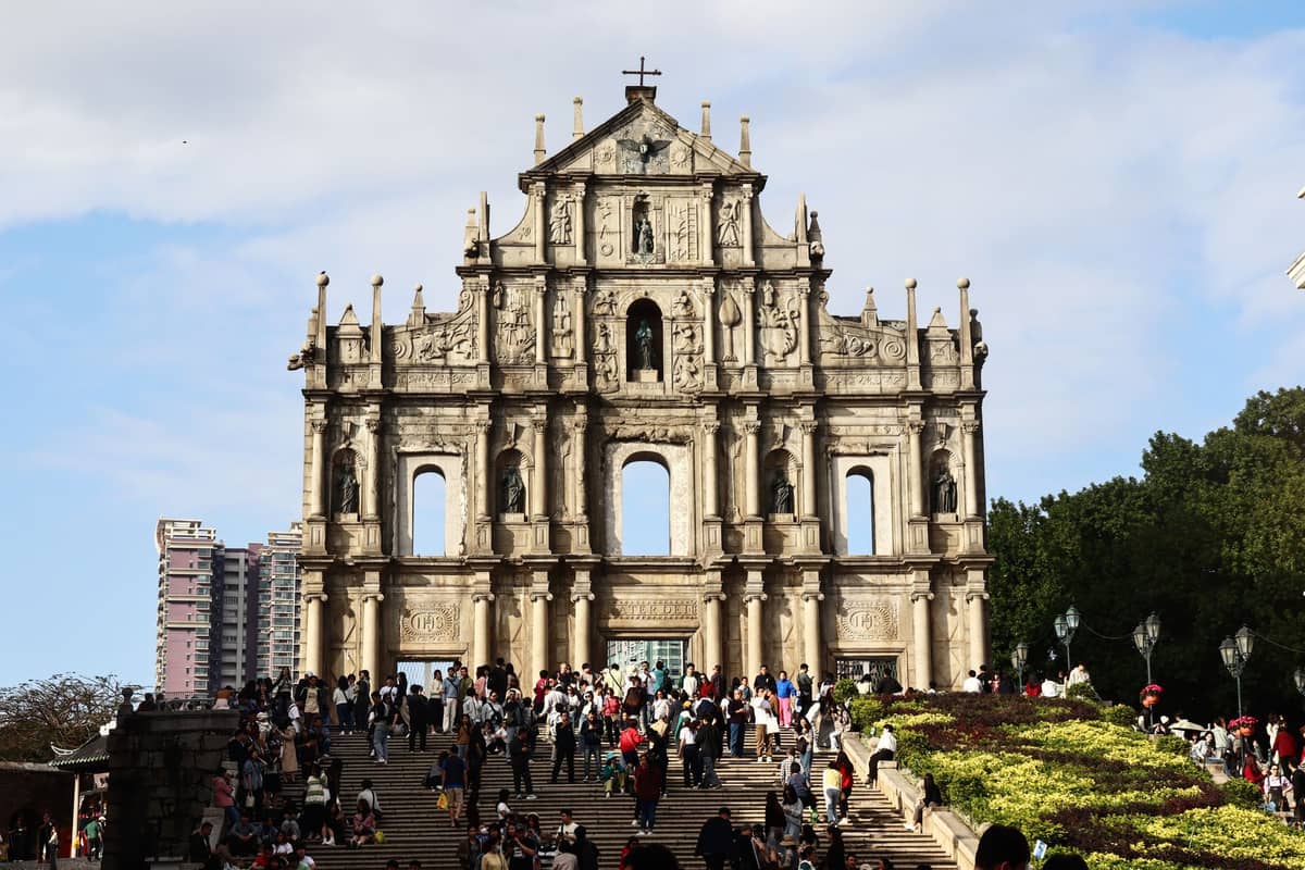 Eine große Menschenmenge versammelt sich an einem sonnigen Tag in Macao vor der historischen Steinfassade der Ruinen von St. Paul's.