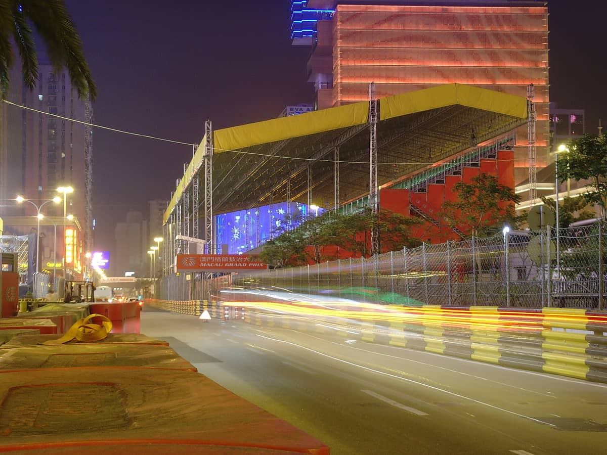 Nachtansicht der Tribünen und der Stadtstrecke des Macau Grand Prix mit sichtbaren Stadtgebäuden und Barrieren.