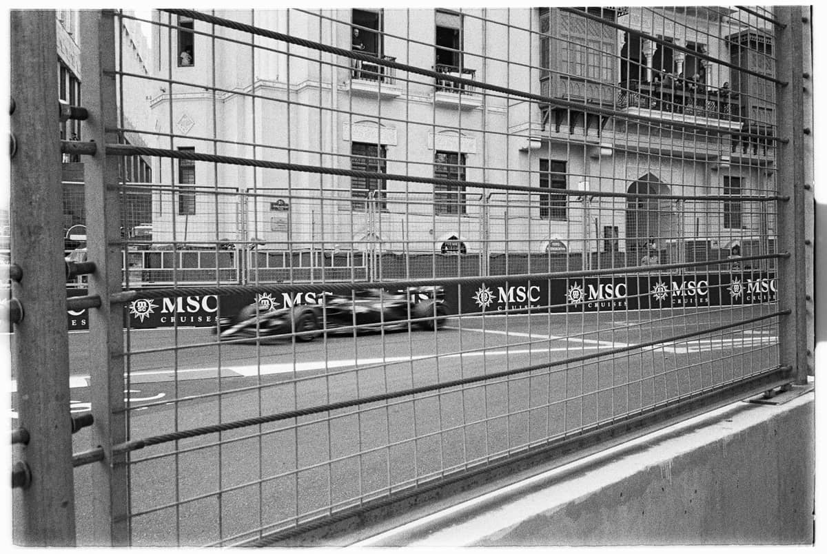 Ein Rennwagen rast beim Macau Grand Prix hinter einer Schutzbarriere durch Stadtstraßen, im Hintergrund historische Gebäude.