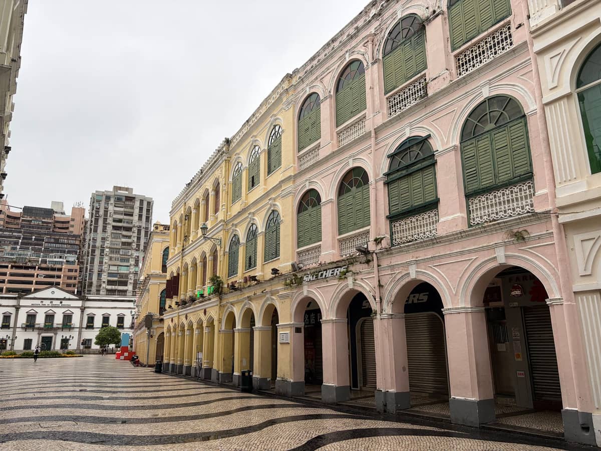 Historische pastellfarbene Kolonialgebäude und das ikonische portugiesische Mosaikpflaster am Senado-Platz, einem UNESCO-Weltkulturerbe im historischen Zentrum von Macau, an einem bewölkten Tag.