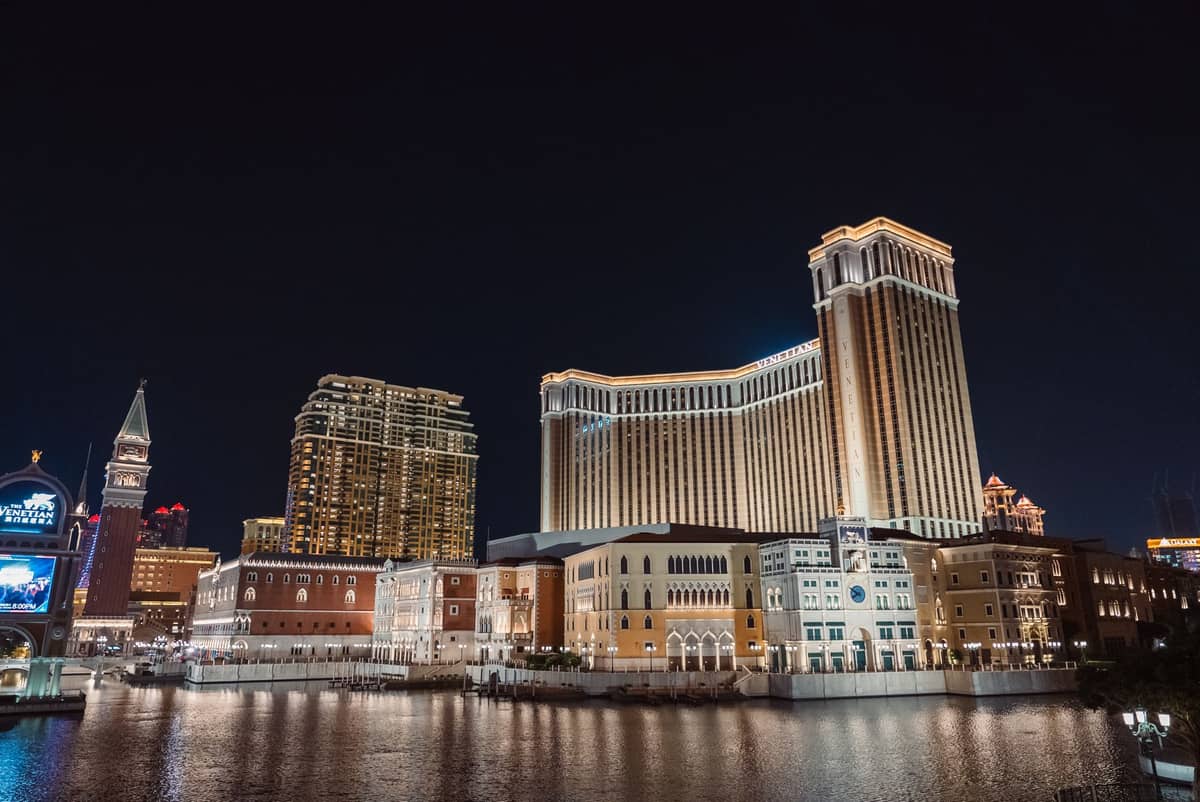 Nachtansicht des Venetian Macao und hell erleuchteter Casinos entlang des Cotai Strip, mit Spiegelungen im Wasser.