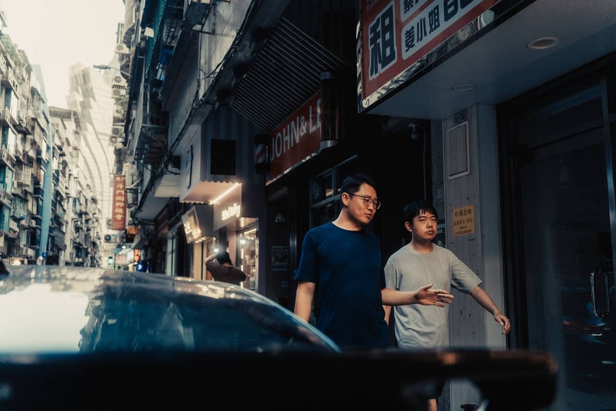 Zwei Personen, die bei Dämmerung an kleinen Geschäften und lokalen Bars in einer engen Straße in Macau vorbeigehen