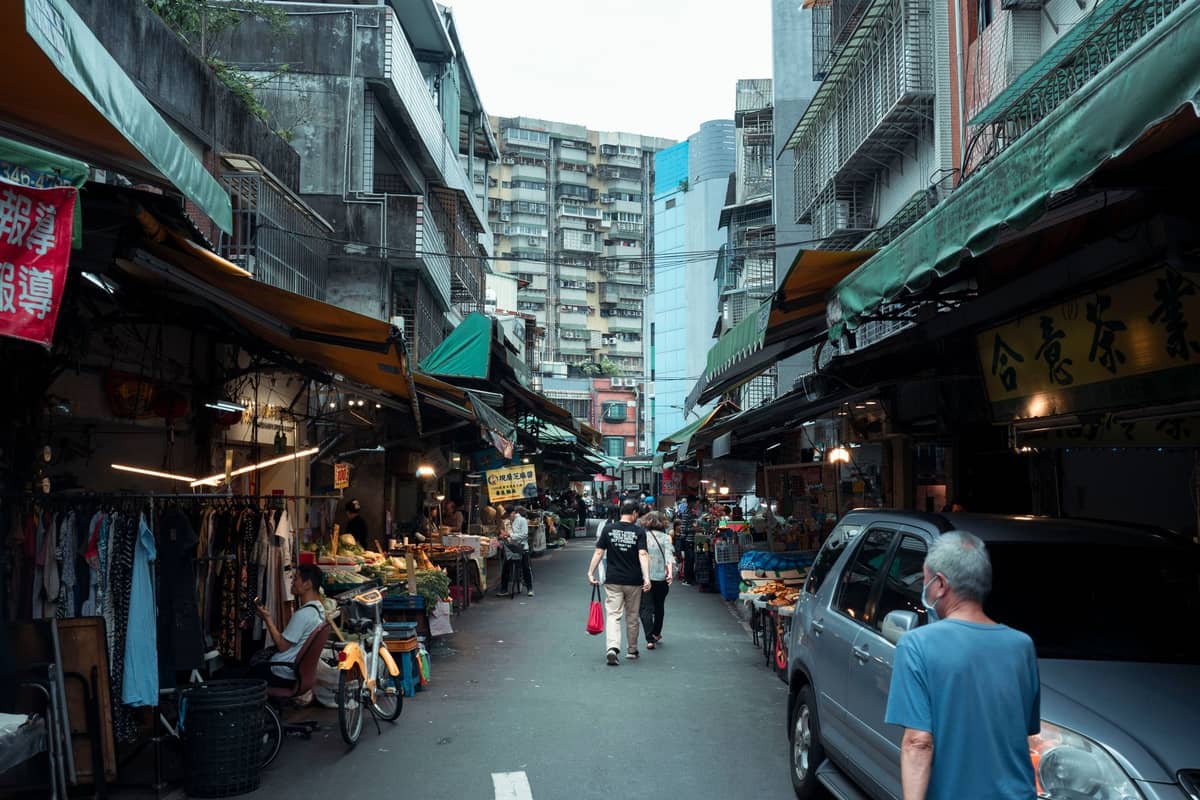 Straße gesäumt von lokalen Geschäften und Essensständen in Macau, mit Fußgängern und Gebäuden, die auf beiden Seiten emporragen.