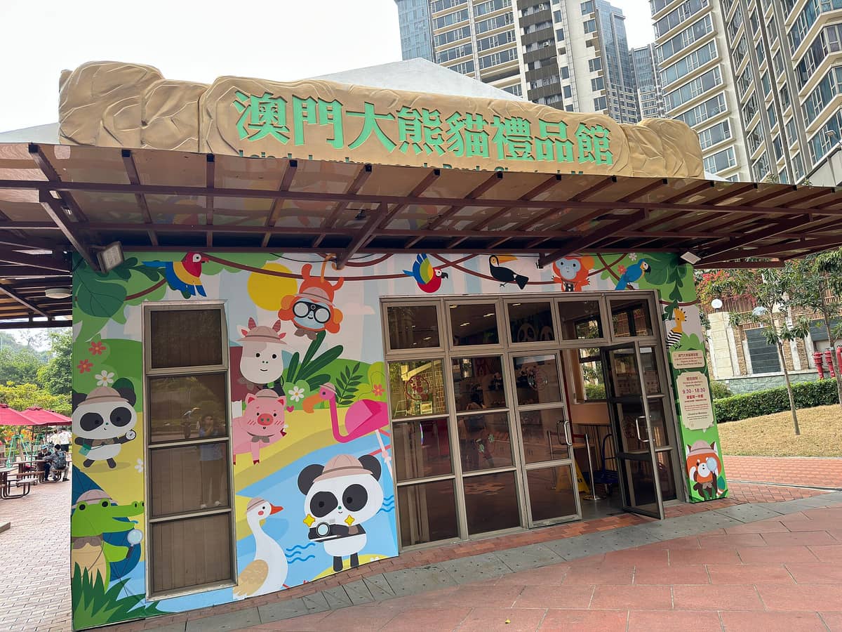 Außenansicht des Souveniershops des Macau Giant Panda Pavilion, mit bunten Cartoon-Pandas und Tieren am Gebäude und hohen Gebäuden im Hintergrund.