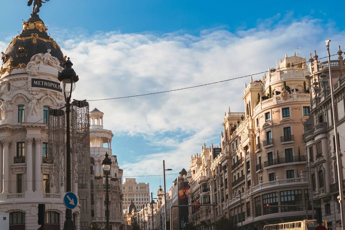 Blick auf die Gran Vía in Madrid mit dem ikonischen Metropolis-Gebäude und eleganten Fassaden aus dem frühen 20. Jahrhundert unter blauem Himmel.