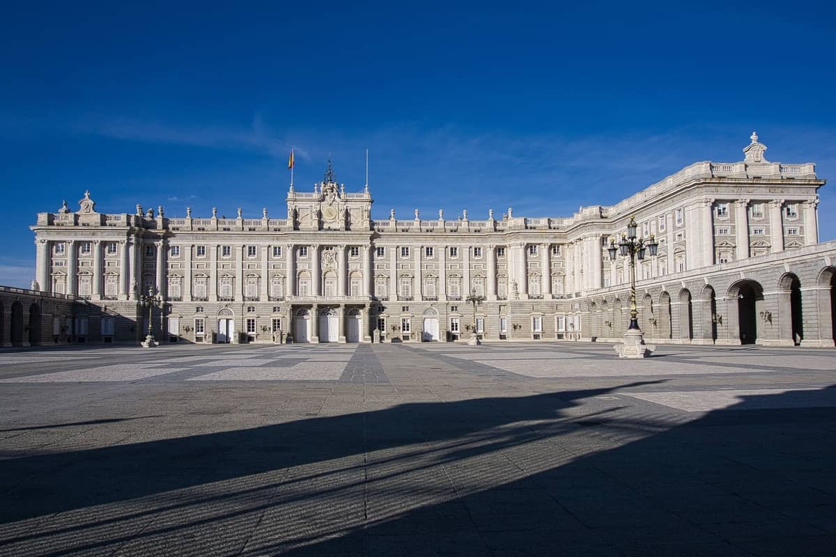 Weitläufige Ansicht des Königlichen Palastes von Madrid mit seiner neoklassizistischen Fassade und dem breiten Innenhof unter einem klaren blauen Himmel.