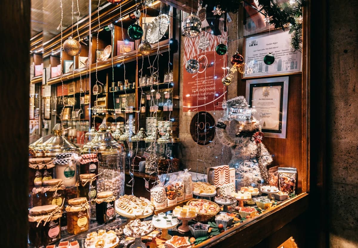 Ein festliches Bäckereifenster in Madrid, gefüllt mit traditionellen Weihnachtssüßigkeiten wie Turrón und Marzipan, geschmückt mit Ornamenten und Lichtern.