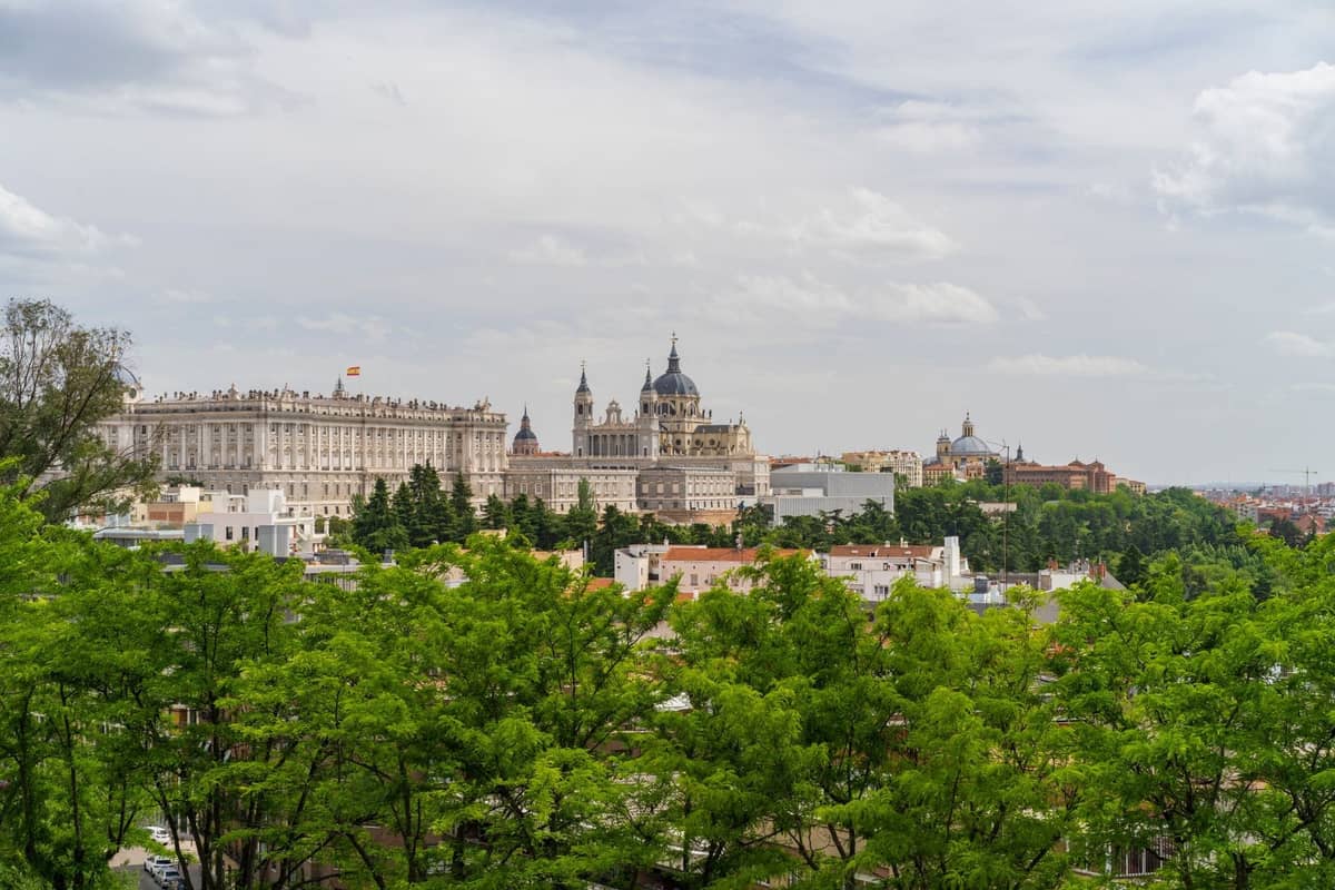 Panoramablick auf Madrid mit der Kathedrale Almudena und dem Palacio Real, umgeben von Gärten und Grünflächen unter einem bewölkten Himmel.