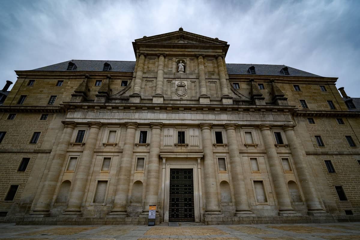 Steinfassade eines imposanten historischen Klosters oder Konvents in Madrid, mit klassischen Säulen, Nischen und einem dramatisch bewölkten Himmel.