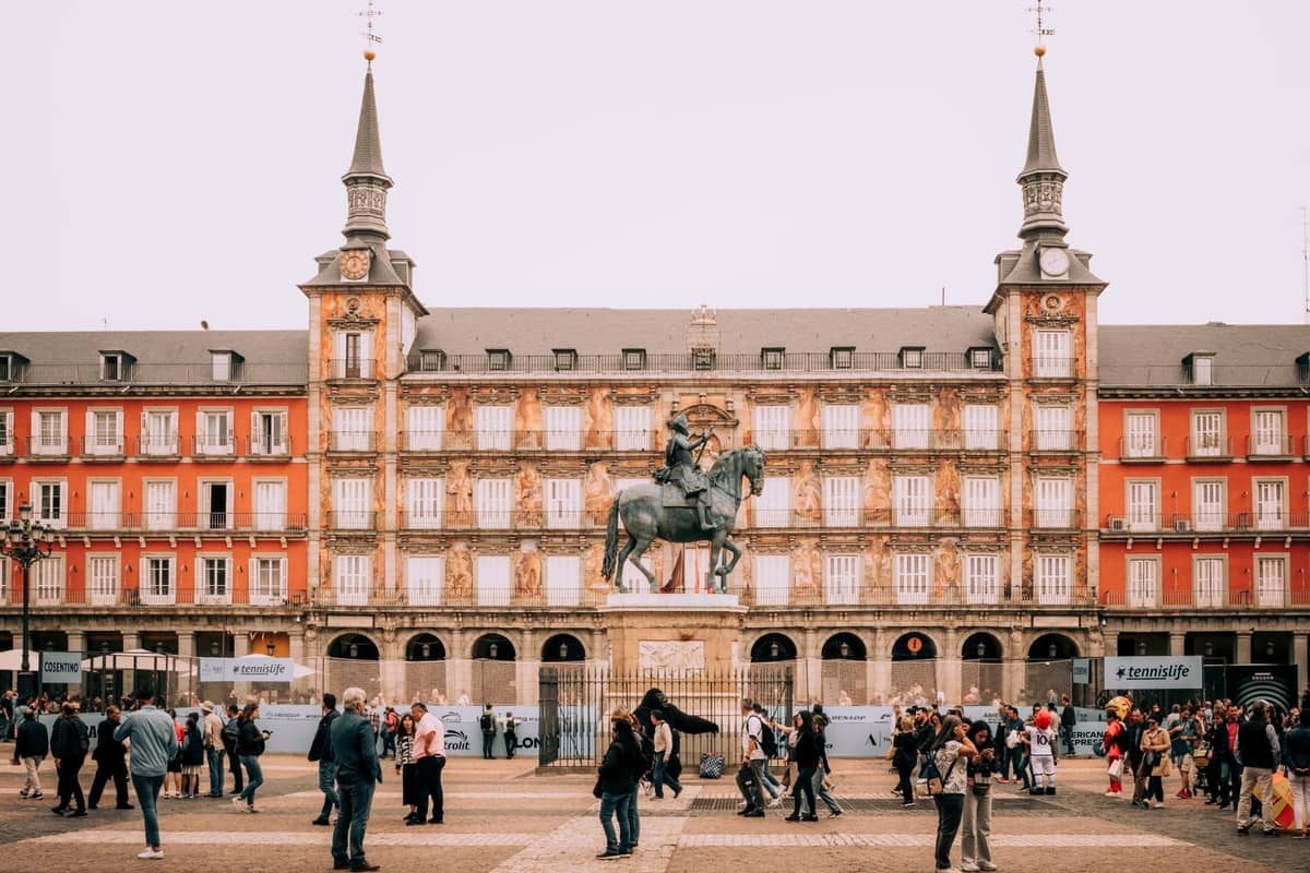 Multitudes se reúnen en la Plaza Mayor de Madrid, una plaza histórica con una estatua en el centro y los icónicos edificios rojos al fondo.