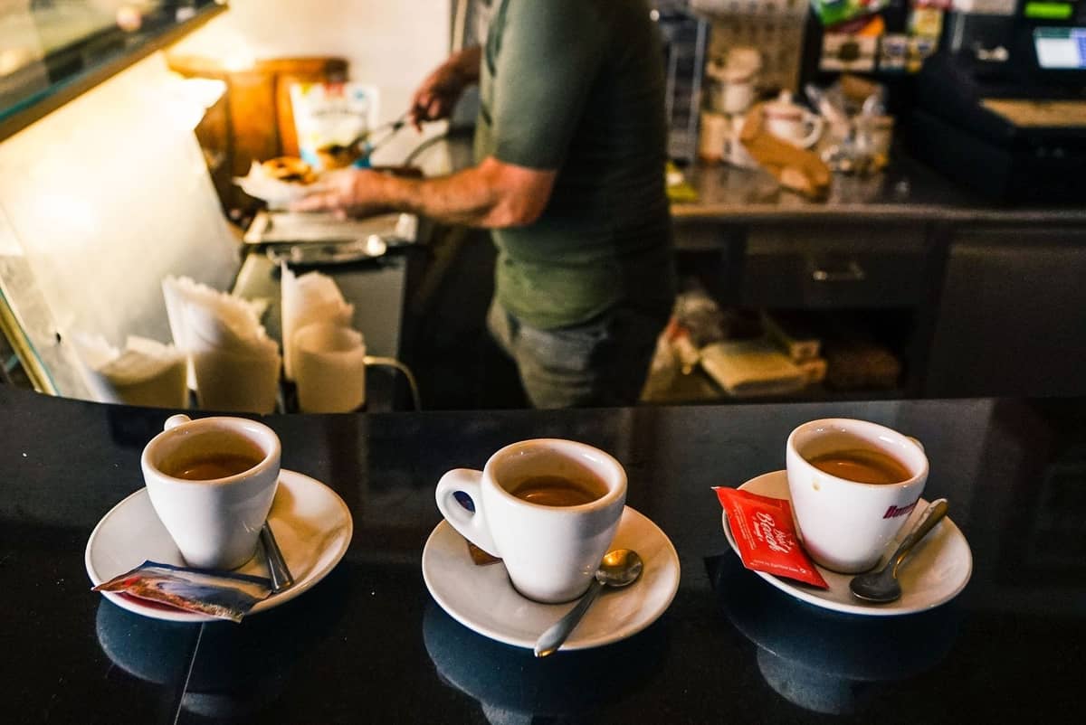 Drei Kaffees auf einem Bartresen mit einer Person, die im Hintergrund Essen zubereitet, typische Morgenszene in einem Café oder einer Bar in Madrid.